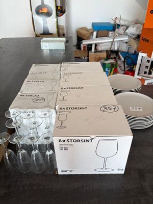 boxes of wine glasses and plates on a table in a cluttered room