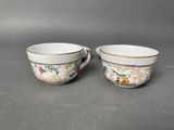 two cups with floral designs and gold rims on them