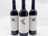 trois bouteilles de vin rouge sont alignées sur une surface blanche