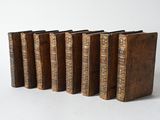 six old books are lined up in a row on a white surface