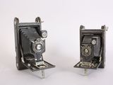 two old cameras sitting side by side on a white surface
