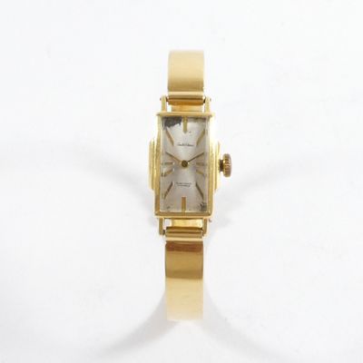 une montre-bracelet en or avec un cadran blanc sur une surface blanche