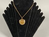 a gold necklace with a coin on a black display stand