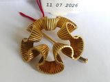 une broche en or posée sur une table blanche, avec une étiquette de prix