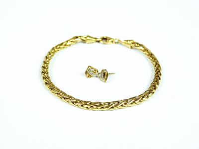 un gros plan d'un bracelet et d'une boucle d'oreille en or posés sur une surface blanche