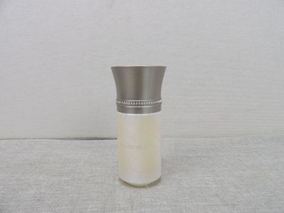 une petite bouteille en verre avec un bouchon argenté, posée sur une surface blanche