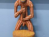 une statue en bois représentant un homme assis sur une chaise