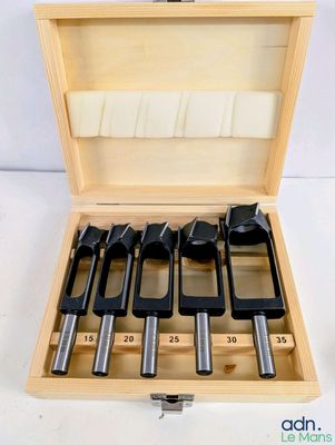 une boîte en bois contenant six outils différents, posée sur une surface blanche