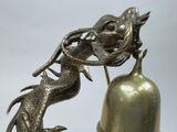 a statue of a dragon on a bell with a bell in the foreground