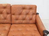 brown leather couch with black legs and arm rests against a white wall