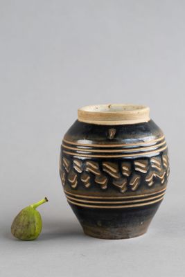un petit vase noir muni d'un couvercle en bois, avec une figurine verte à côté