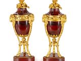 une paire de vases anciens rouges et dorés posés sur des socles, sur une surface blanche