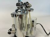 a silver coffee maker with a glass of water in front of it