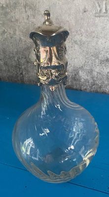 un vase en verre transparent avec un couvercle doré, posé sur une table bleue