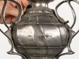 a person holding a silver vase on a table