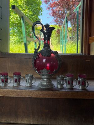 a red vase and cups sitting on a wooden shelf