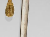 a silver and gold dagger with a bell hanging from it ' s end