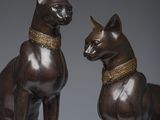 two bronze statues of cats sitting next to each other on a gray surface
