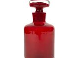 une bouteille en verre rouge avec un bouchon argenté, posée sur une surface blanche