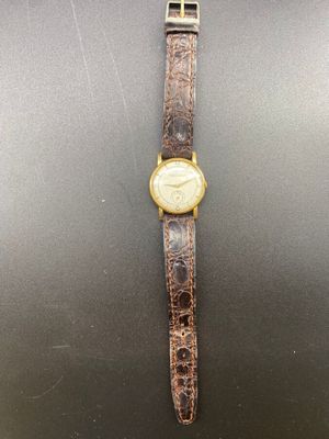 une montre en or avec un bracelet en cuir marron sur un fond noir