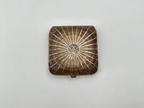 un petit objet métallique carré orné d'un motif en forme d'étoile rayonnante
