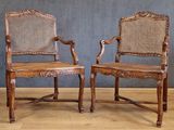 two wooden chairs with wicker back and arms against a gray wall