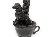 statue of two dogs sitting in a cup on a white surface