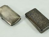 two silver cigarette cases sitting next to each other on a white surface