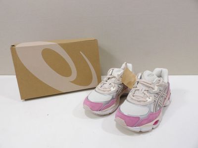 Des baskets roses et blanches sont posées sur une surface blanche, à côté d'une boîte en carton