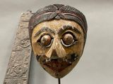 a wooden mask on a stick with a ruler in the background