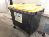 a black trash can with a yellow lid sitting on a sidewalk