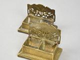 two small brass objects sitting on a white surface