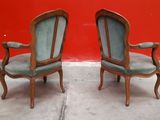 pair of antique chairs with upholstered armrests against a red wall
