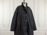 Le manteau noir est suspendu à un support de mannequin.