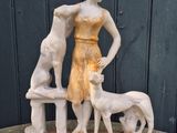 statue of a woman and two dogs on a bench in front of a black wall