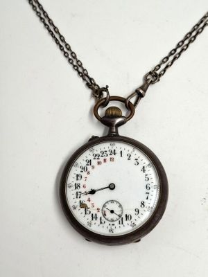 une montre de poche ancienne avec une chaîne, posée sur une surface blanche