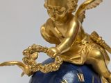 a blue and gold clock with an angel sitting on top of it