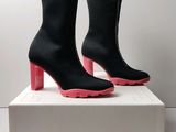 une paire de bottes noires aux semelles roses posée sur une boîte