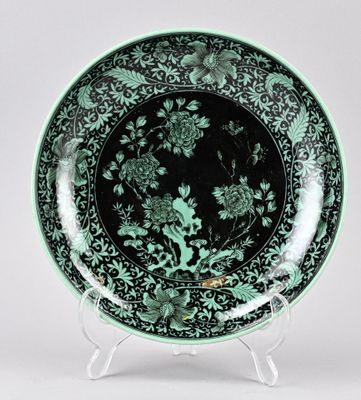 assiette verte et noire décorée de fleurs et d'oiseaux, posée sur un socle