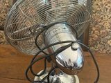 a silver fan sitting on a wooden table in front of a chair