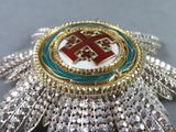 silver, gold, and red broochle with a cross on it