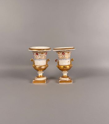 paire de vases dorés et blancs munis d'anses et posés sur des socles
