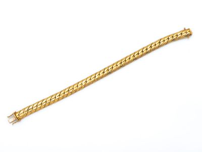 un bracelet en or posé sur une surface blanche, sur fond blanc