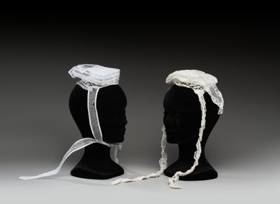 une paire de têtes de mannequins noires coiffées de bonnets blancs et ornées d'un ruban blanc