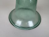 a green glass vase with a black lid on a white table