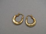 une paire de boucles d'oreilles créoles en or posées sur une surface grise