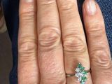 a woman ' s hand with a diamond and emerald ring on it