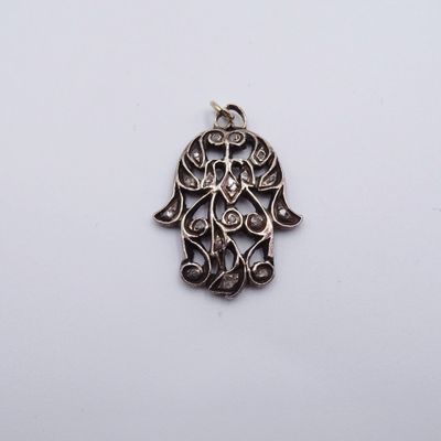 un pendentif en forme de hamsa en argent, orné d'un motif finement ouvragé sur fond blanc