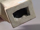 a hand holding a small square object with a hole in it