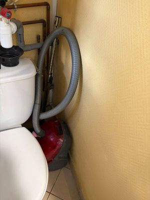 a white toilet with a vacuum in the corner of a bathroom